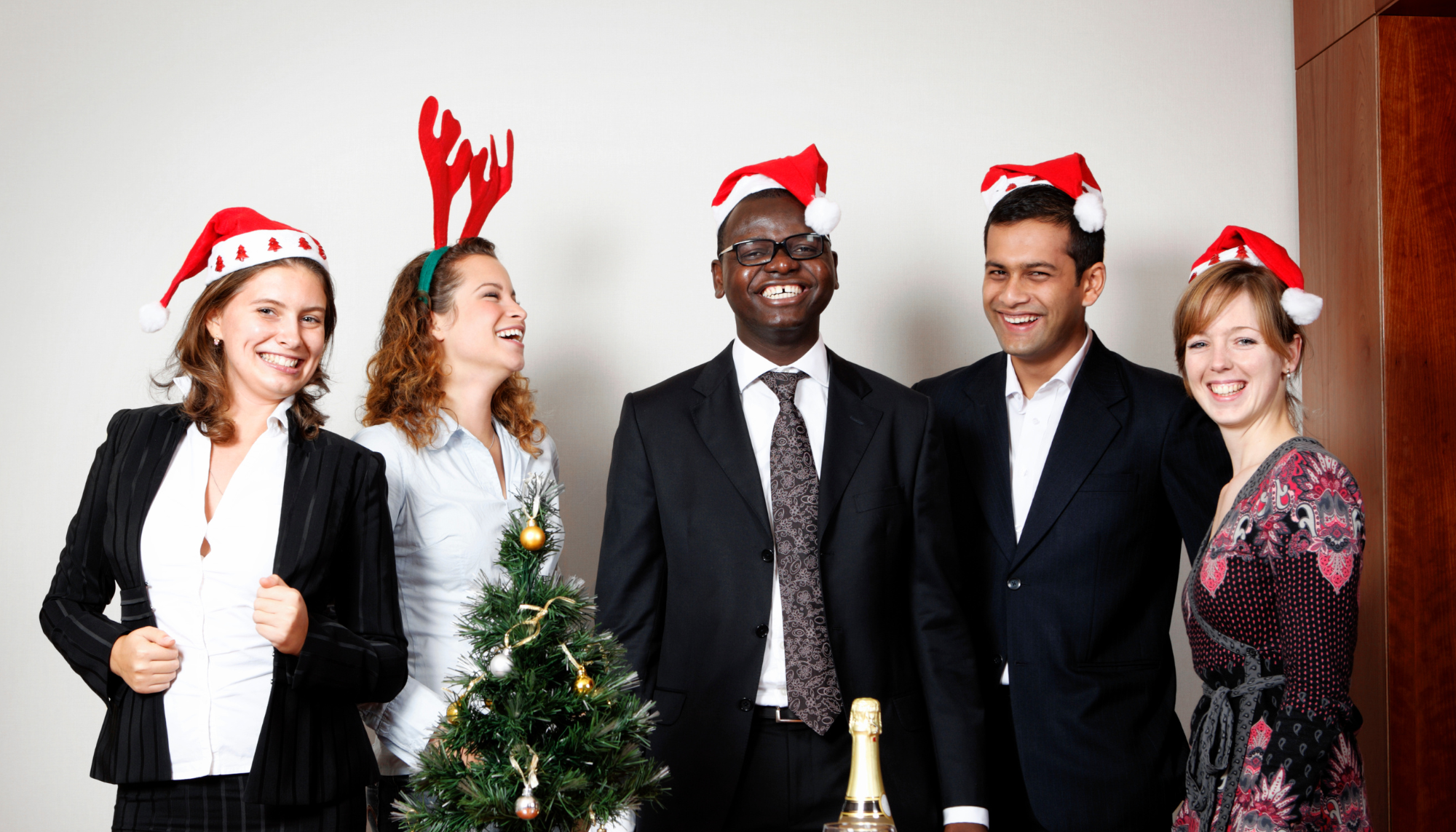 5 people laughing and standing in smart uniform wearing Christmas hats
