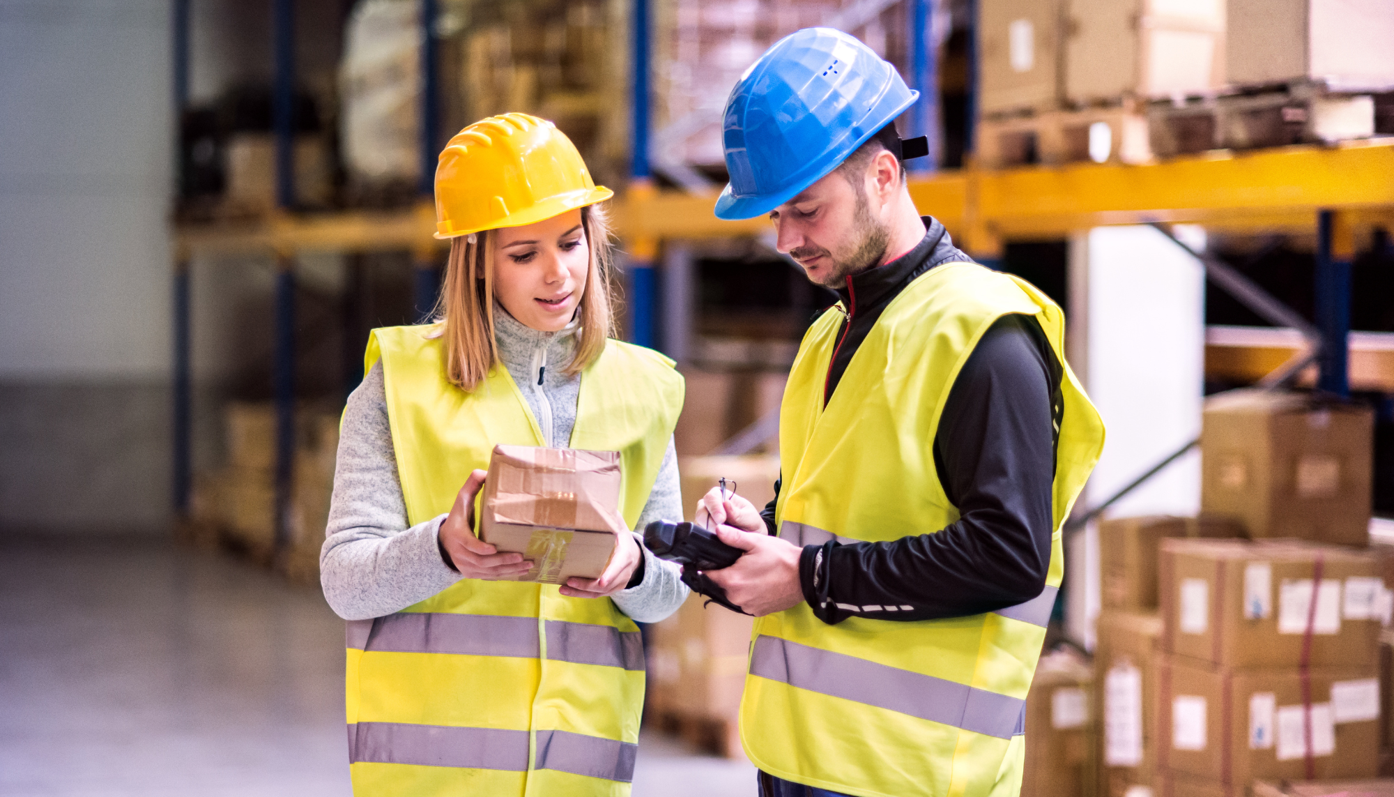man and women in high visbility clothing and hard hats in a warehouse or manufacturing factory looking at a small tablet